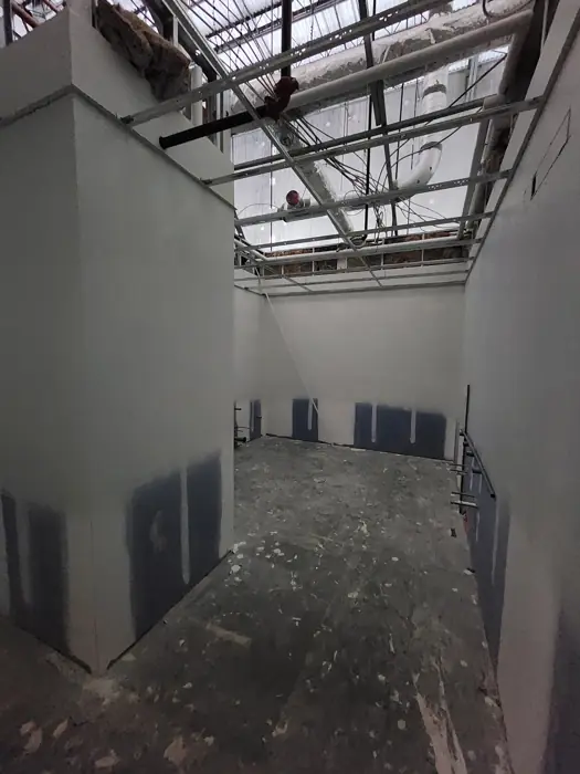 Tall drywall walls with open ceiling grid and primed patches