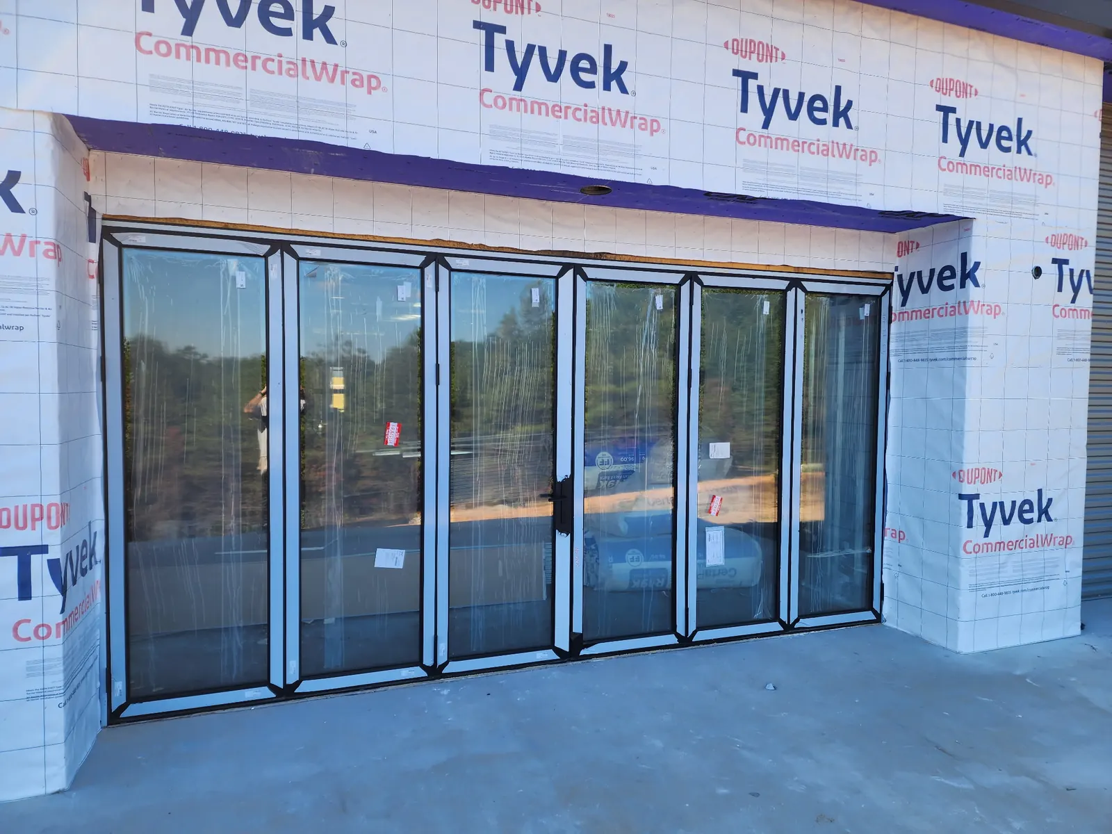 Bifold glass storefront doors installed in a Tyvek-wrapped commercial opening