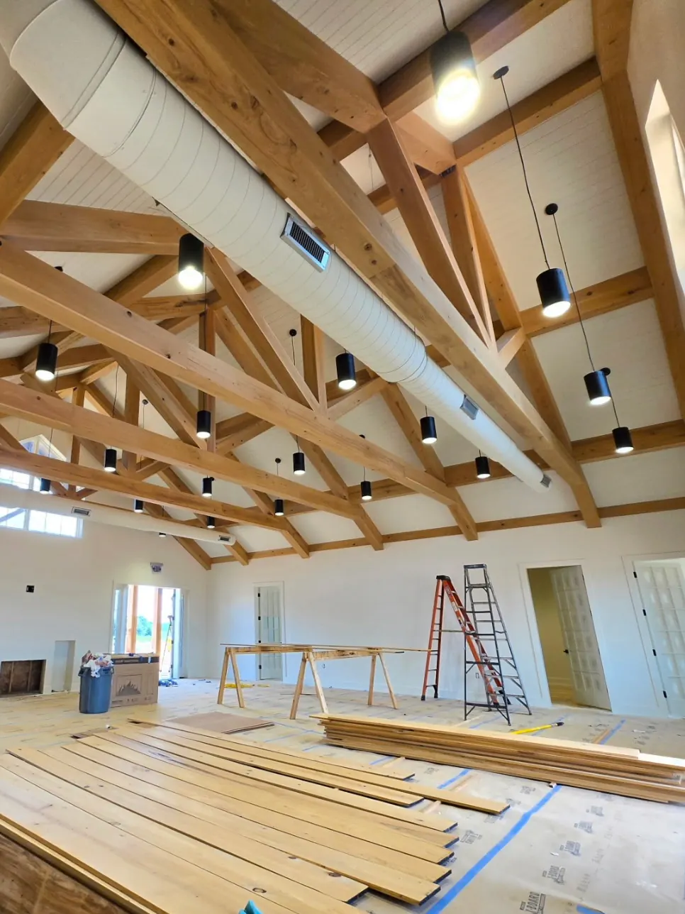 Timber-beam vaulted commercial interior with pendant lighting and new flooring going in